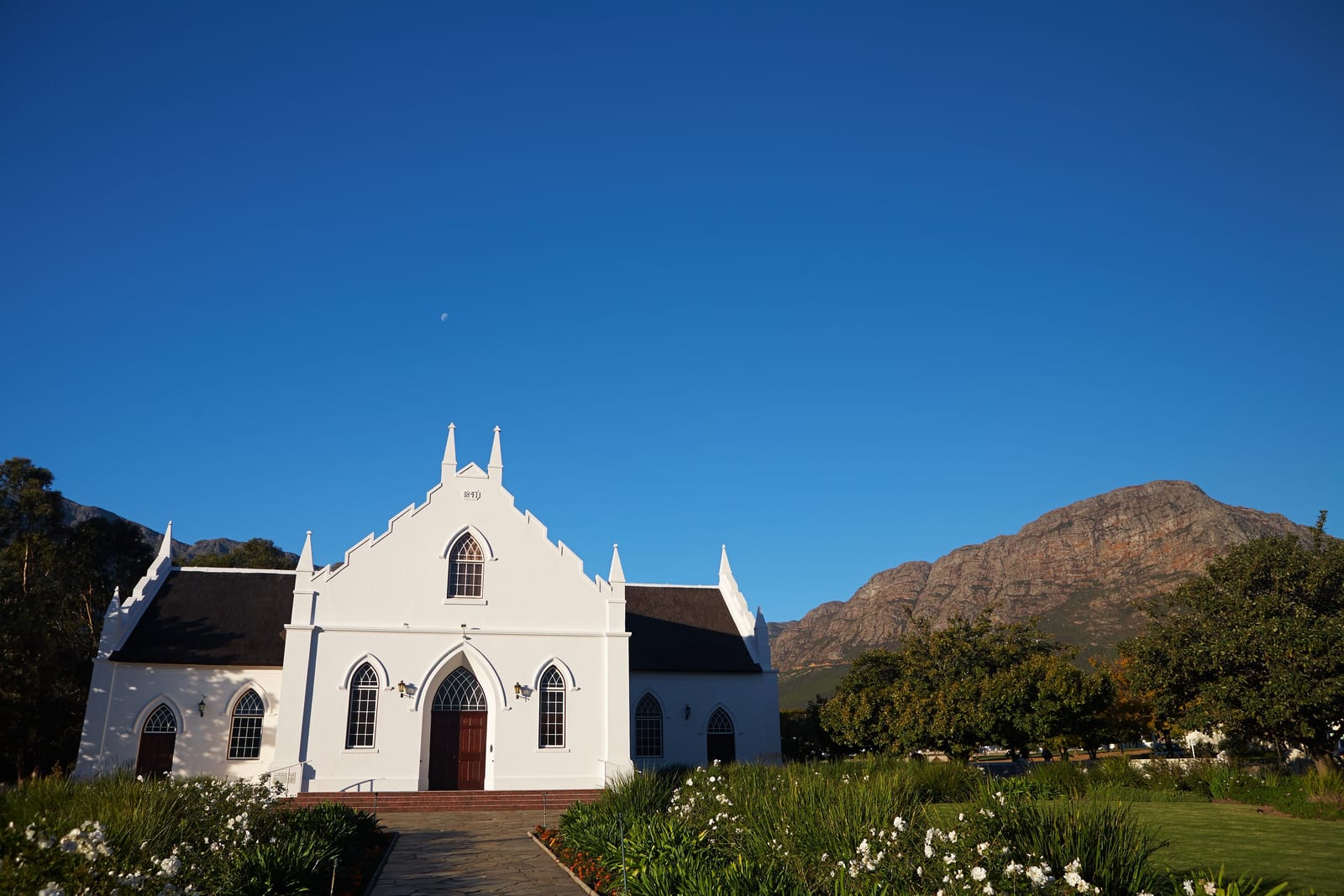 Weiße Kirche mit geschwungenen Giebeln vor den Bergen von Franschhoek