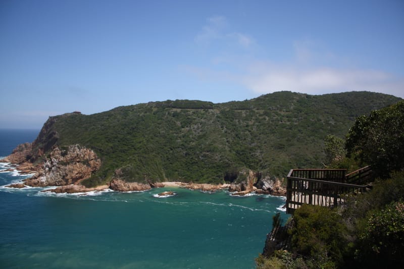 Bewaldete Felsküste über einer türkisen Bucht an den Knysna Heads