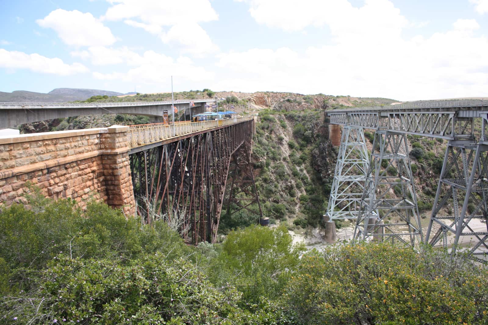 Alte Steinbrücke und eiserne Gitterbrücke über eine Flussschlucht, dahinter eine moderne Betonbrücke
